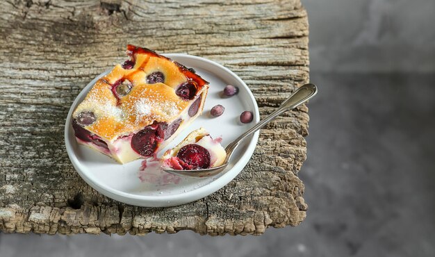 Ein Stück hausgemachter Clafoutis-Kirsche-Torte, ein traditionelles französisches Dessert auf einem grauen Teller