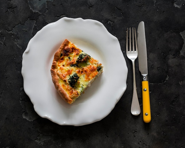 Ein Stück Kuchen mit Brokkoli, Hühner, Spinat und Käse auf einem dunklen Hintergrund