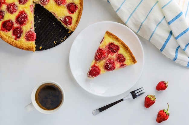 Ein Stück Kuchen mit Erdbeeren und und Kokosnuss und Teebecher auf dem Tisch.