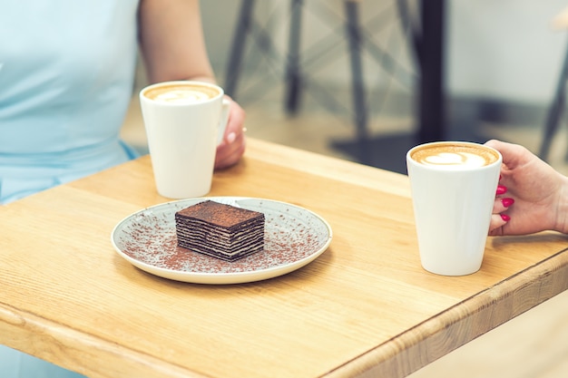 Ein Stück leckerer Schokoladenkuchen auf dem Tisch auf Hintergrund der Hände mit Tassen Kaffee.