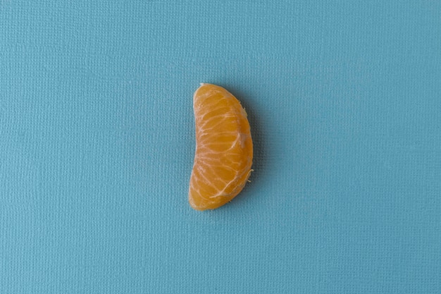 Ein Stück Mandarine auf pastellblauem Hintergrund. Die Mandarine liegt in der Mitte.