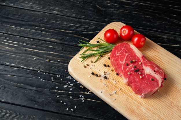 Ein Stück saftiges rohes Rindfleisch auf einem Schneidebrett auf einem schwarzen Holztischhintergrund.