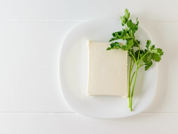 Ein Stück serbischer Käse mit einem kleinen Blatt Petersilie auf einem weißen Tisch. Der Blick von oben. Milchprodukt. Flach liegen.