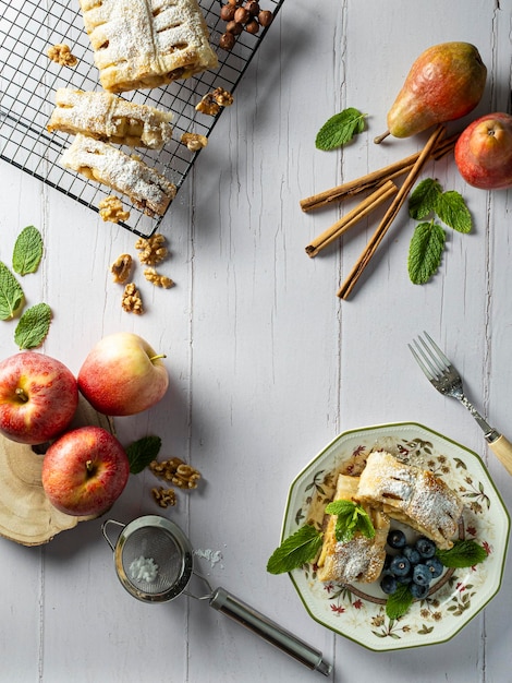 Ein Stück traditioneller Apfelstrudel mit Puderzucker-Minz-Preiselbeeren und Zimt im Vordergrund auf einer Tischplatte