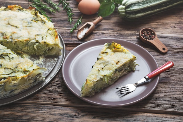 Ein Stück Zucchinikuchen gebacken mit Parmesan-Eiern und Kräutern auf dem Teller auf dem Holztisch in der Nähe