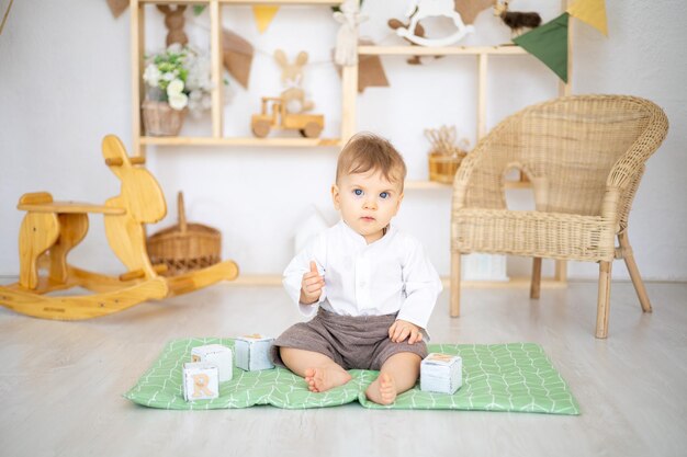 Ein süßer, gesunder Junge spielt mit hölzernen Lernspielzeugen in einem hellen, gemütlichen Kinderzimmer zu Hause vor dem Hintergrund eines Holzhauses