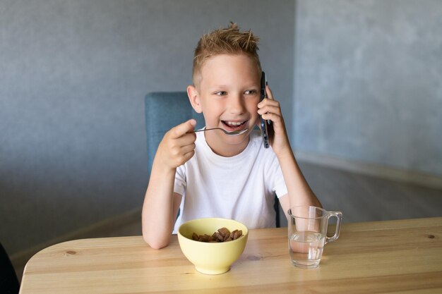 Ein süßer Junge frühstückt und telefoniert Ein Glas Wasser