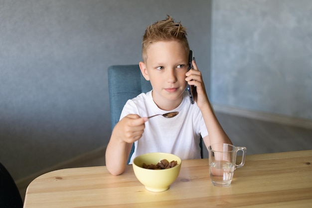 Ein süßer Junge frühstückt und telefoniert Ein Glas Wasser