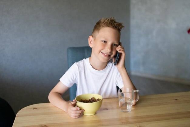 Ein süßer Junge frühstückt und telefoniert Ein Glas Wasser