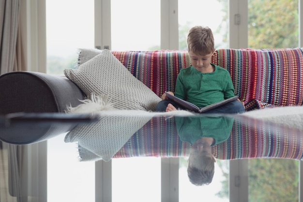 Foto ein süßer junge liest ein buch auf dem sofa in einem bequemen zuhause