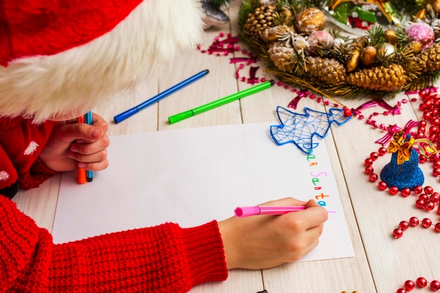 Foto ein süßer junge mit weihnachtsmannshut schreibt einen brief an den weihnachten