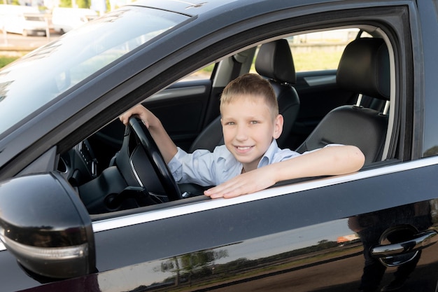 Ein süßer Junge sitzt hinter dem Steuer eines Autos und lächelt