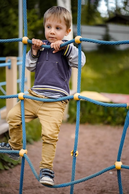 Ein süßer kaukasischer kleiner Junge, der die Netzausrüstung auf dem Spielplatzbild mit selektivem Fokus hochklettert