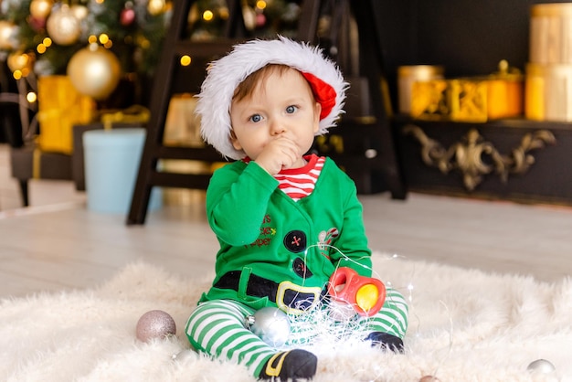 Ein süßer kleiner Junge, der als Elf verkleidet ist, öffnet ein Weihnachtsgeschenk in einem geschmückten Weihnachtshaus.