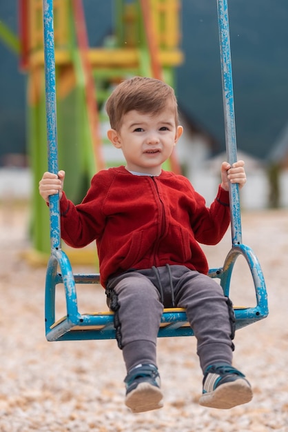 Ein süßer kleiner Junge, der auf einer Schaukel auf einem Spielplatz im Sommerpark spielt