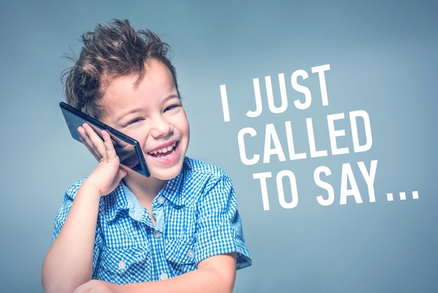 Ein süßer kleiner Junge in einem blauen Hemd spricht am Telefon neben der Inschrift I JUST CALLED TO SAY