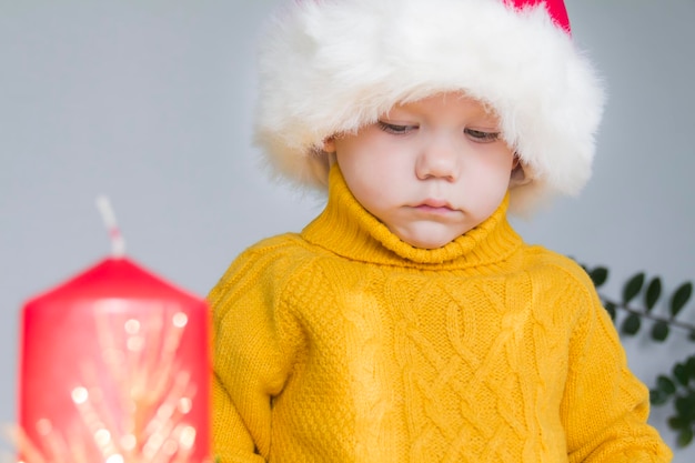 Ein süßer kleiner Junge in einem gelben Pullover und einem roten Weihnachtsmann-Hut mit einer roten Weihnachtskerze