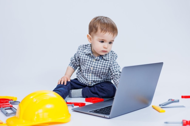 Ein süßer kleiner Junge in einem karierten Hemd sitzt auf einem weißen Hintergrund mit einem Laptop Kinderspielzeug