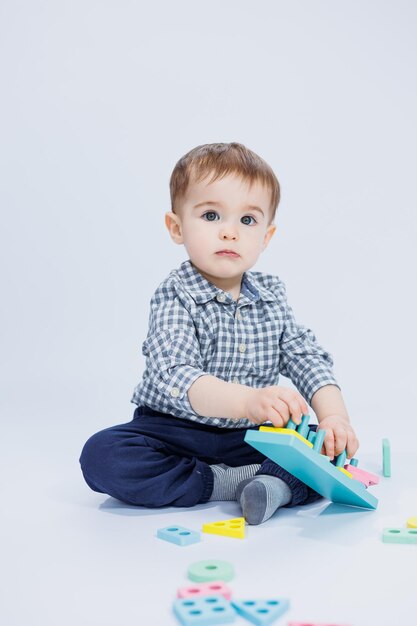 Ein süßer kleiner Junge in einem karierten Hemd sitzt auf weißem Hintergrund und spielt mit Lernspielzeug aus Holz Ökologisches Holzspielzeug für Kinder