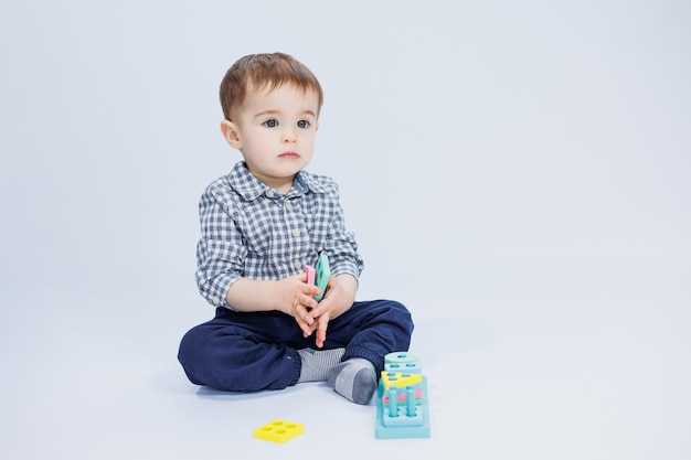 Ein süßer kleiner Junge in einem karierten Hemd sitzt auf weißem Hintergrund und spielt mit Lernspielzeug aus Holz Ökologisches Holzspielzeug für Kinder