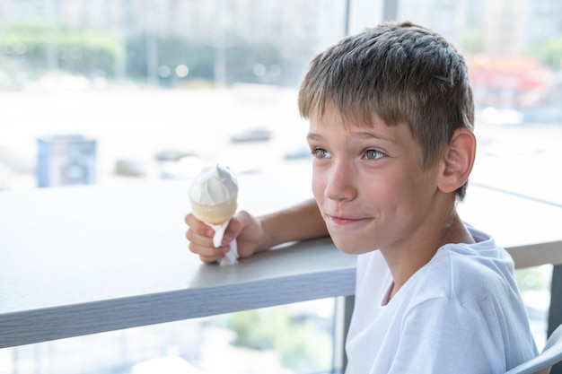 Ein süßer Teenager isst ein wirbelndes weißes Eis in einem Waffelbecher, der an einem Tisch am Fenster in einem Café sitzt