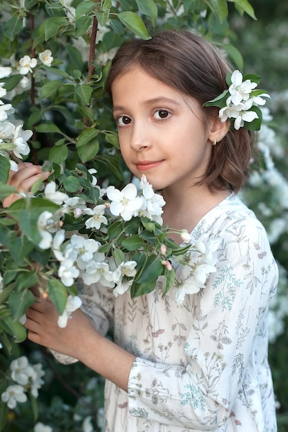 Ein süßes 9-jähriges Mädchen mit großen schönen Augen und einem leichten Kleid in blühenden weißen Apfelbäumen Frühlingsspaziergänge im blühenden Garten Apfelblüte