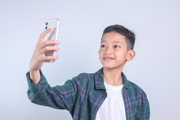 Ein süßes asiatisches Kind in Freizeitkleidung macht ein Selfie, um es an Freunde und Anhänger zu schicken.