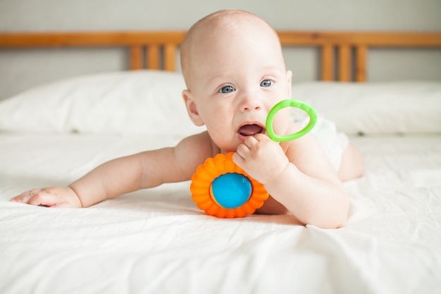 Ein süßes Baby liegt auf einem weißen Laken und spielt fröhlich mit einer hellen Rassel