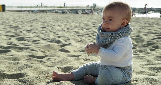 Foto ein süßes baby sitzt am sandstrand gegen den himmel