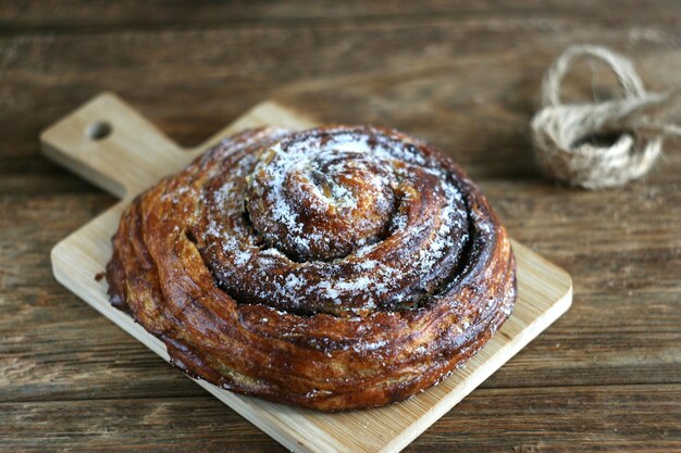 Ein süßes Brötchen mit Schokolade und Zimt liegt auf einem Holzbrett auf dem Tisch Das Brötchen ist mit Pulver selektiven Fokus bestreut