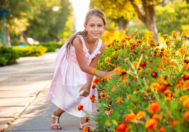 Ein süßes charmantes Mädchen in einem schönen rosa Kleid schnüffelt feurige Ringelblumen in einem hellen Park an einem sonnigen Tag in einem lang erwarteten Urlaub