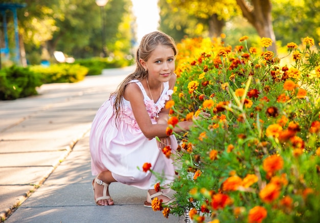 Ein süßes charmantes Mädchen in einem schönen rosa Kleid schnüffelt feurige Ringelblumen in einem hellen Park an einem sonnigen Tag in einem lang erwarteten Urlaub