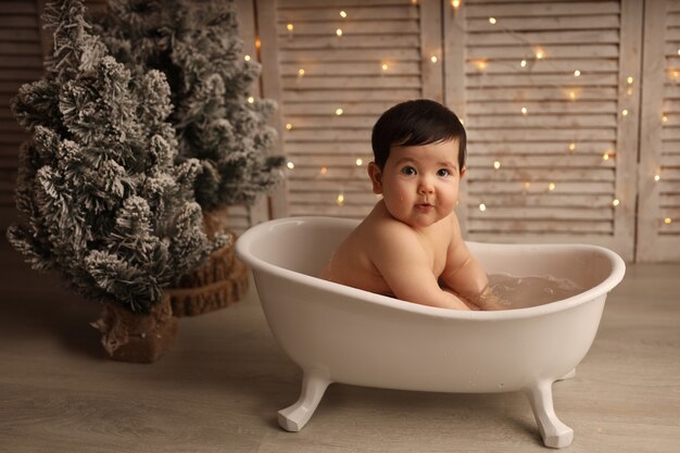 Ein süßes dunkelhäutiges Mädchen sitzt in einer Badewanne mit Weihnachtsbaumspielzeug