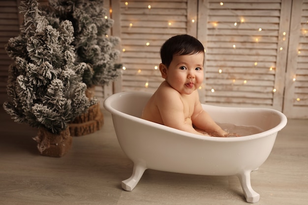 Ein süßes dunkelhäutiges Mädchen sitzt in einer Badewanne mit Weihnachtsbaumspielzeug