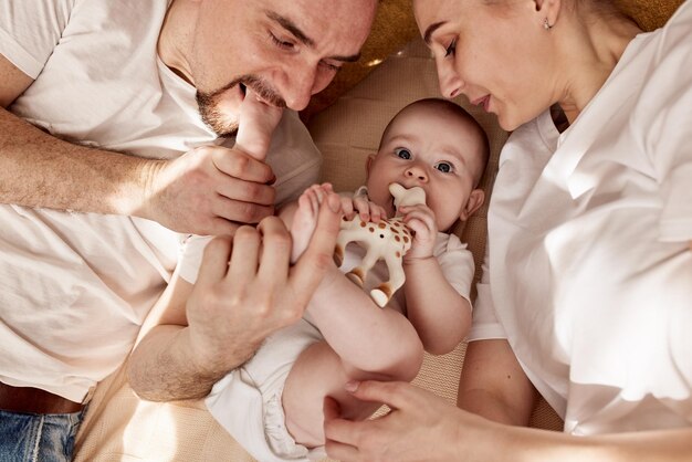 Ein süßes, fröhliches Baby und seine Eltern liegen auf dem Boden in einem hellen, gemütlichen Zimmer mit Spielzeug, Mama und Papa umarmen sich