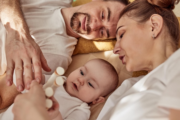 Ein süßes, fröhliches Baby und seine Eltern liegen auf dem Boden in einem hellen, gemütlichen Zimmer mit Spielzeug, Mama und Papa umarmen sich