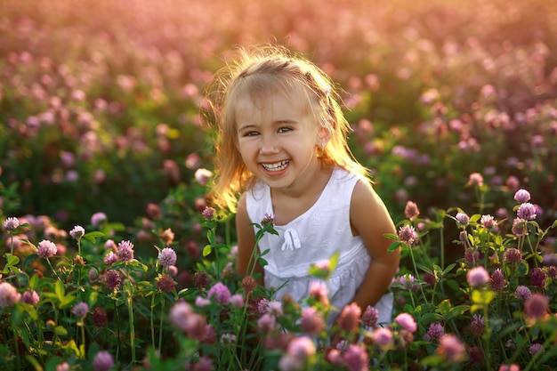 Ein süßes, glückliches kleines Mädchen auf einem Feld mit Kleeblumen lacht fröhlich