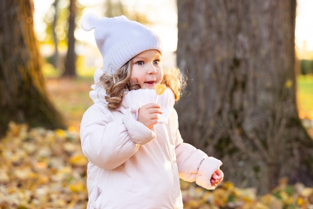 Ein süßes hübsches Mädchen ruht sich mitten im Herbstlaub im Park aus und probiert einen Lutscher