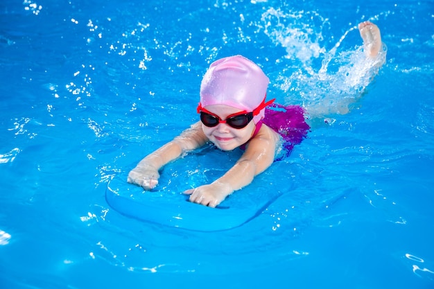 Ein süßes Kind im Vorschulalter lernt mit einem Flutterboard im Innenpool zu schwimmen