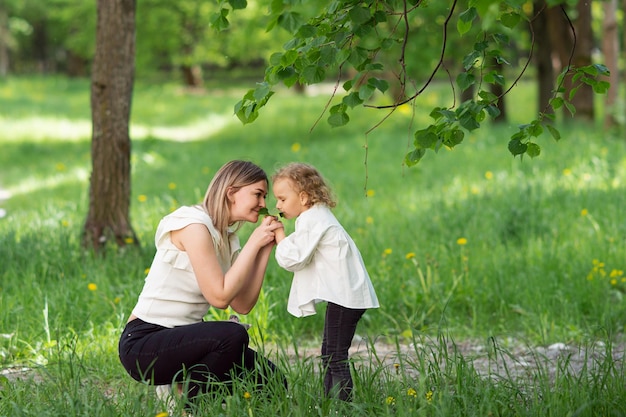 Ein süßes Kind steht neben seiner Mutter und bläst auf einen weißen Löwenzahn