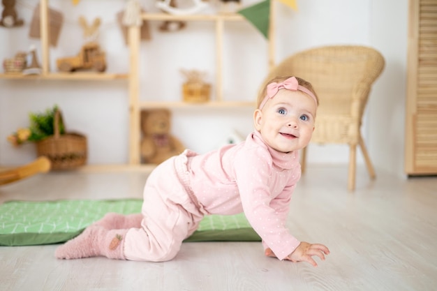 Ein süßes kleines gesundes Mädchen bis zu einem Jahr in einem rosafarbenen Anzug aus natürlichem Stoff sitzt auf einem Teppich in einem Kinderzimmer mit hölzernen Lernspielzeugen, die lächelnd auf die Kamera schauen