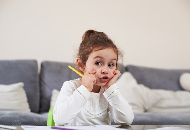 Ein süßes kleines Mädchen, das an einem Tisch sitzt und einen gelben Stift in ihren Händen hält