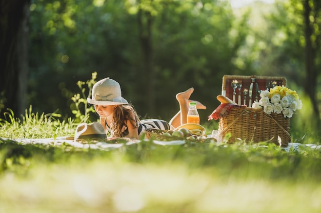Ein süßes kleines Mädchen, das auf der Decke auf einem Gras liegt und einen Frühlingstag mit einem Picknick verbringt.