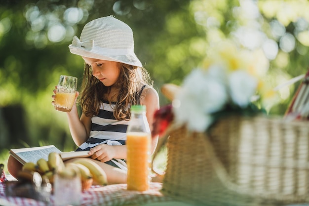 Ein süßes kleines Mädchen, das einen Frühlingstag in der Natur verbringt und ein Buch über ein Picknick liest.