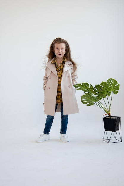 Ein süßes kleines Mädchen im Trenchcoat steht auf weißem Hintergrund Fashion Childhood