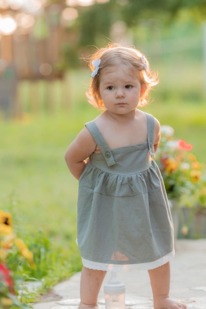 Ein süßes kleines Mädchen in einem grünen Baumwoll-Sommerkleid geht im Sommer bei Sonnenuntergang barfuß bei Sonnenuntergang spazieren