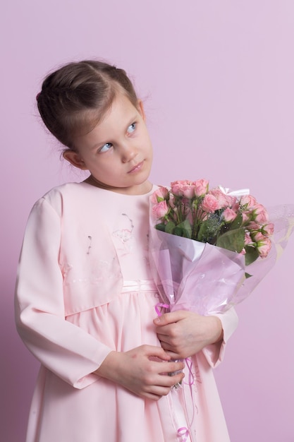 Ein süßes kleines Mädchen in einem rosa Kleid hält einen Blumenstrauß mit rosa Rosen