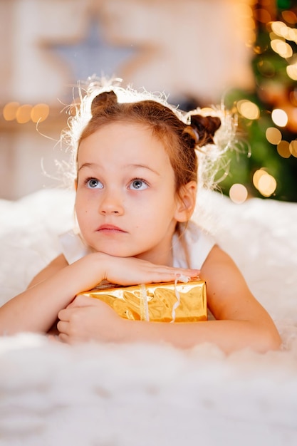 Ein süßes kleines Mädchen in einem weißen Kleid mit einem Geschenk in goldenem Geschenkpapier