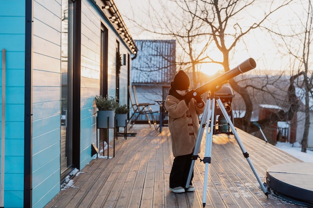 Ein süßes kleines Mädchen mit einem astronomischen Teleskop, das die Sterne unter einem sonnigen Himmel beobachtet.