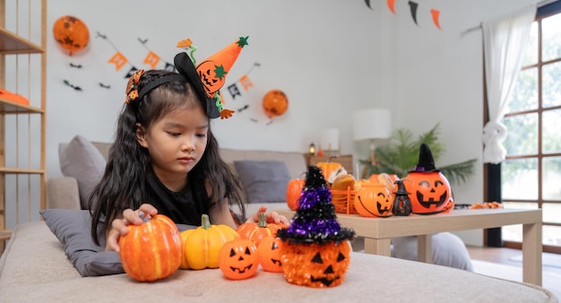 Ein süßes kleines Mädchen mit einem Kürbisballon, eine glückliche Familie, die sich auf Halloween vorbereitet.